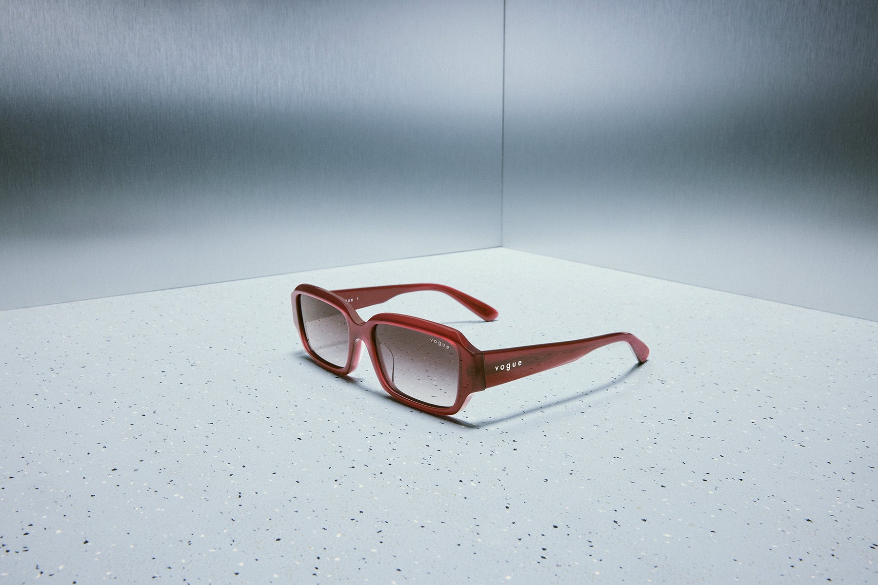 Official Vogue Eyewear still life, red sunglasses against brushed steel